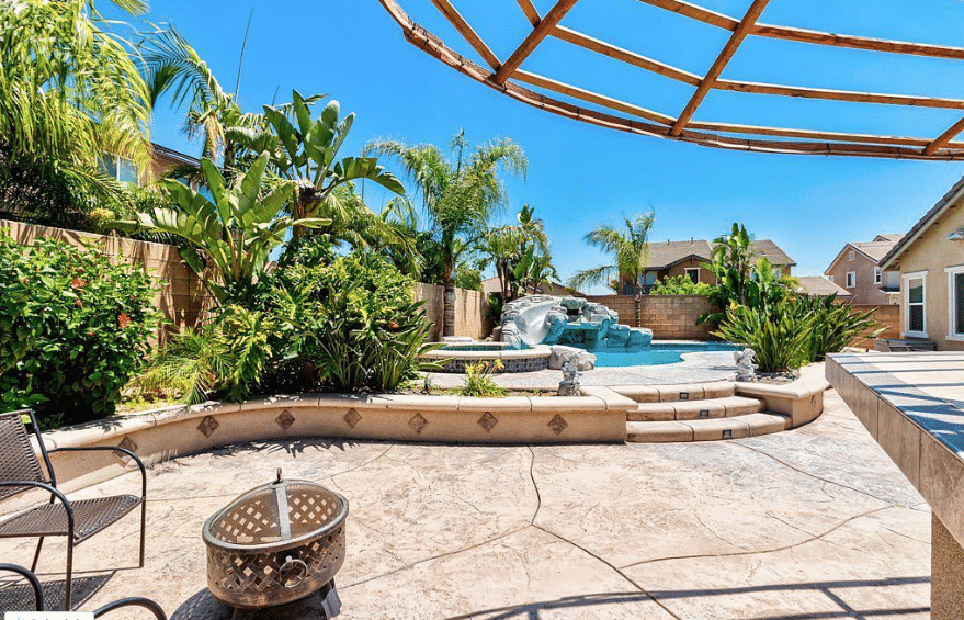 backyard with a rock pool with slide surrounded by lush tropical landscaping 