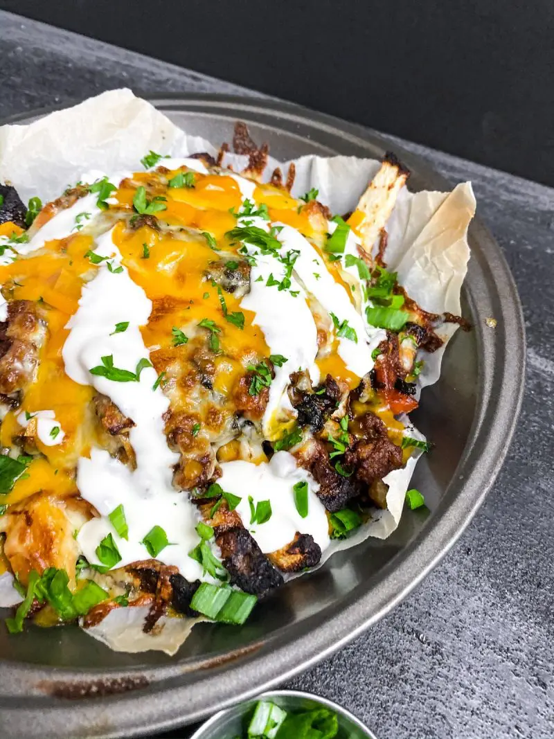 Round pan full of Keto Chili Cheese Fries on a black background.