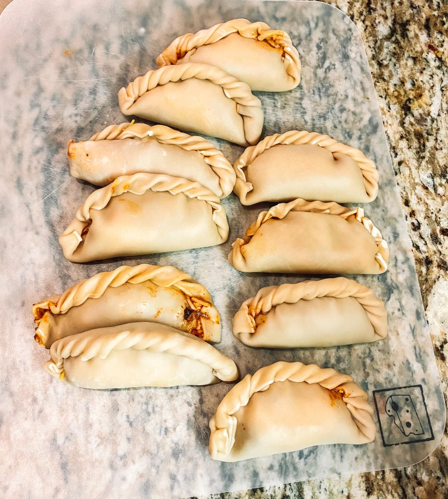 uncooked sealed and crimped empanadas on a cutting board