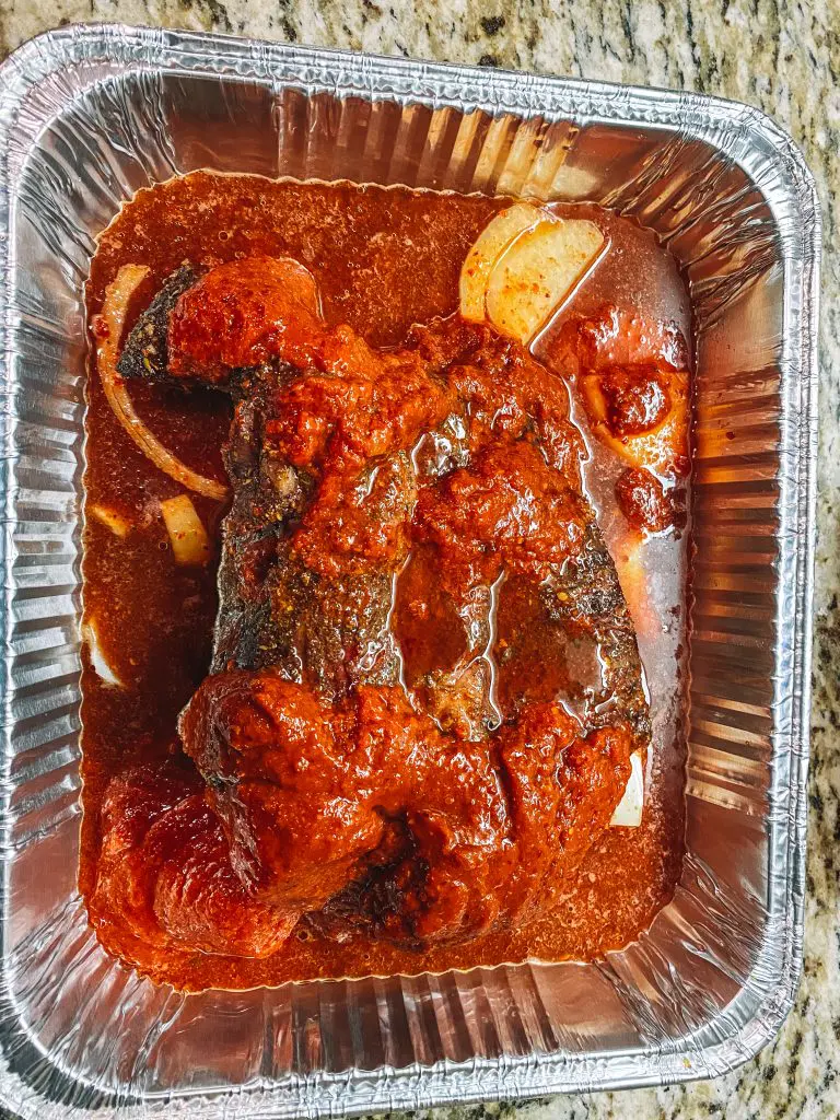 finished braising smoked beef barbacoa with barbacoa sauce and onions in an aluminum pan